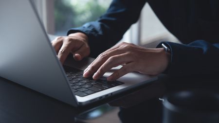 A close up photo of someone's hands while typing on a laptop