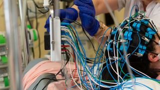 close up photo of a medical provider's gloved hands as they adjust colorful wires that are stuck to a hospitalized patient's head