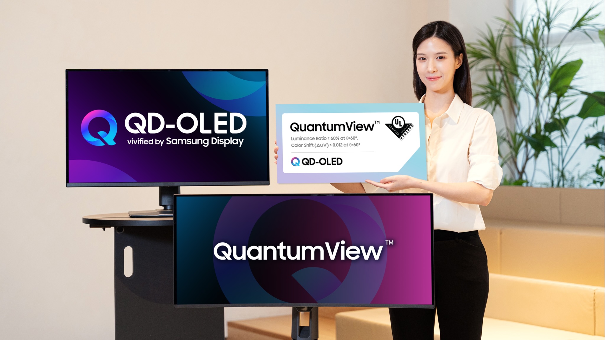 A model poses next to two samsung displays to promote Samsung QD-OLED QuantumView certification