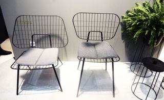 A black wire frame dining and lounge chair with grey book shaped cushions.