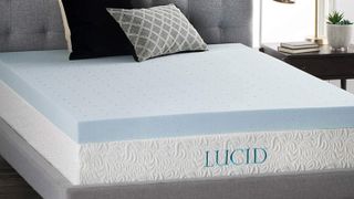 The blue Lucid 4 Inch Gel Mattress Topper placed on a white mattress and dressed with cushions
