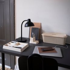 IKEA HÖNSNÄT cable management box on a black desk with a black lamp, notebook, phone and other organisers 