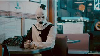 En clown sitter på ett café och tittar obehagligt på något i Terrifier