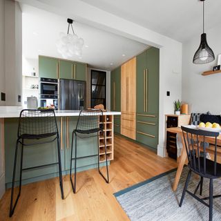 kitchen with white pendant lights, green cabinets, wooden flooring, wooden dining table, black and wire stools