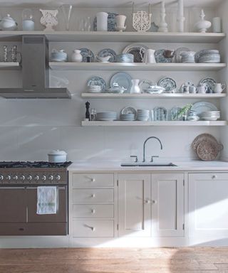 A white kitchen with four layers of open shelving displaying white kitchenware