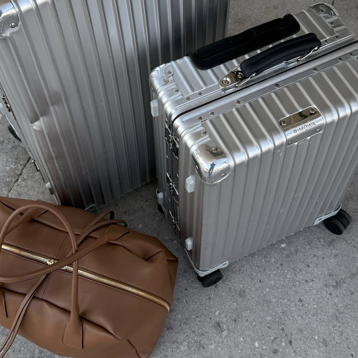 Rimowa suitcases next to a brown leather duffel bag
