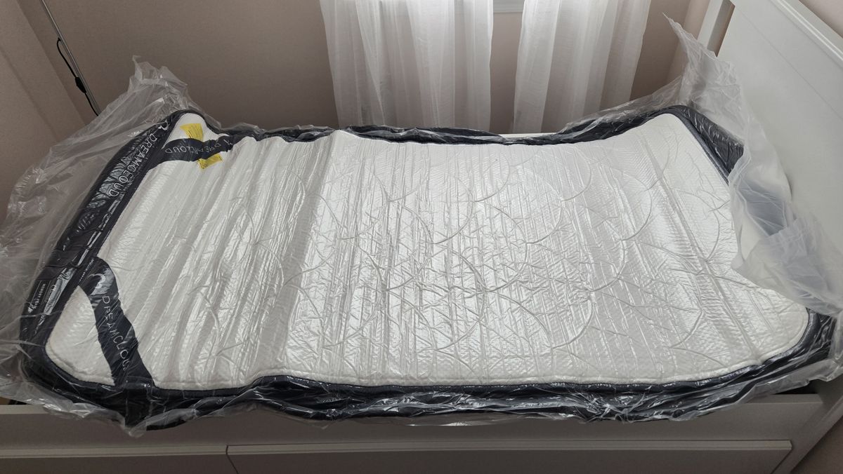 DreamCloud Classic Memory Foam Mattress unrolled but still flat and wrapped in plastic on a platform bed