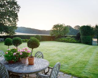 view over garden furniture on terrace across lawn to cloud pruned evergreens and countryside beyond garden