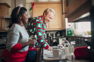 Man washing dishes at Christmas as wife stands with glass of wine