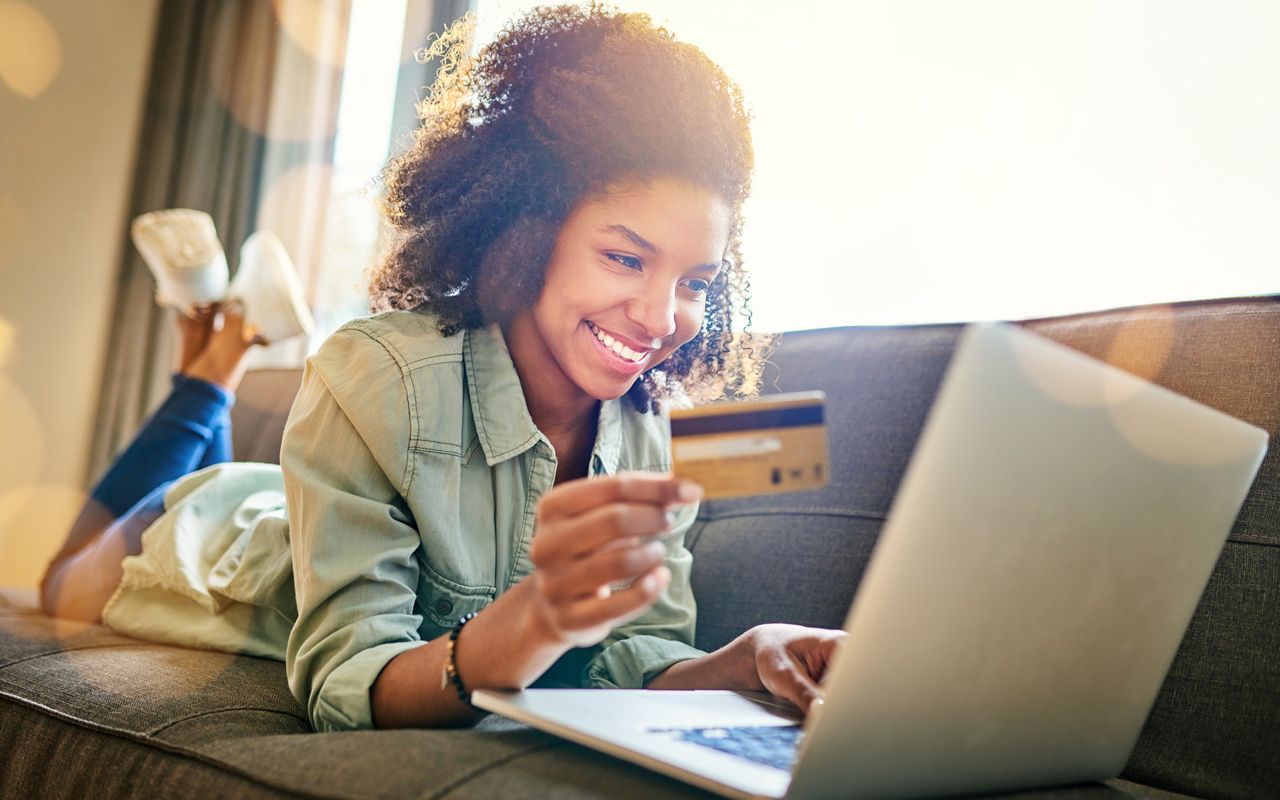 Shot of a cheerful young woman doing online shopping while lying on a couch at home during the day