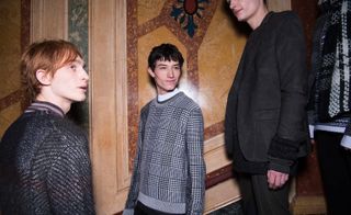 Three male models wearing looks from Pringle of Scotland's collection. One model is wearing a grey piece with a striped high neck top underneath. Another model is wearing a grey patterned jumper. And the third model is wearing a dark grey suit and black jumper