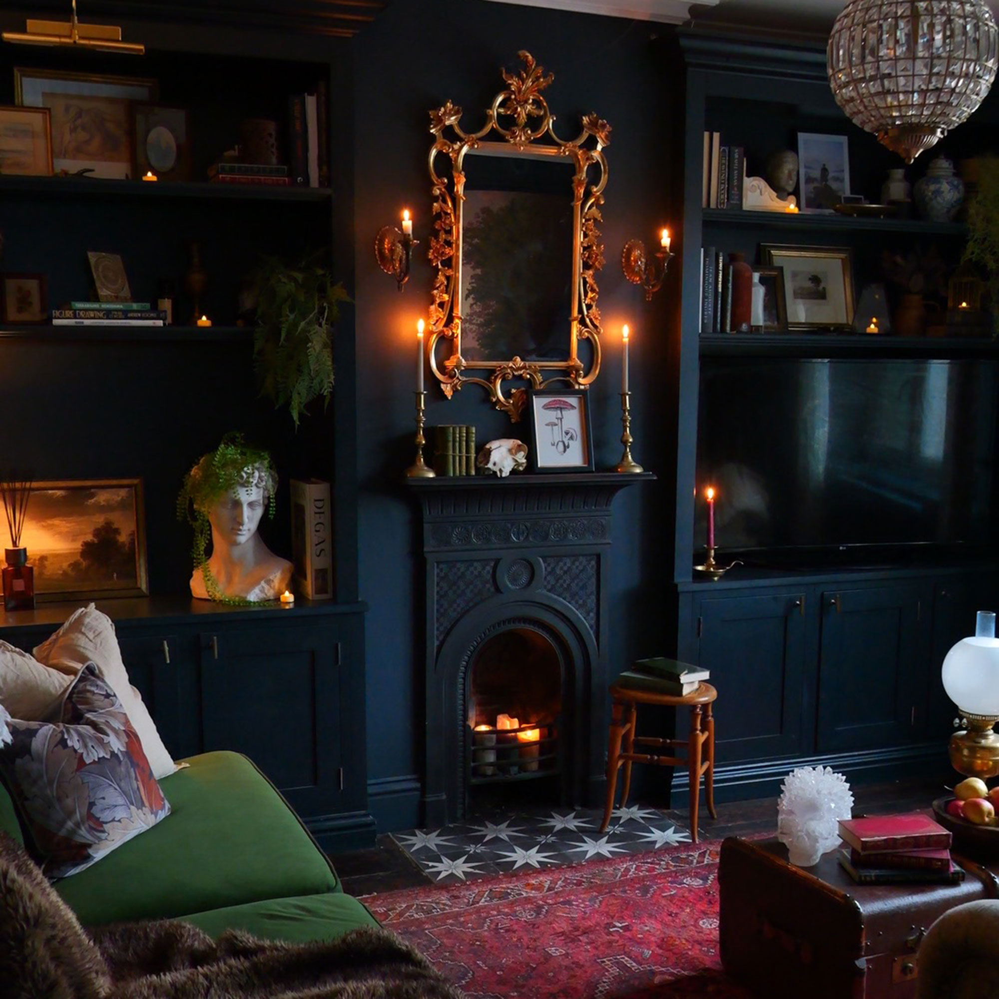 Dark blue living room with gilt mirror, black iron fireplace, rug Oriental rug, chandelier and books on shelves