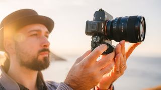 Sony A7 IV being hels by a man with a beard wearing a hat by the sea