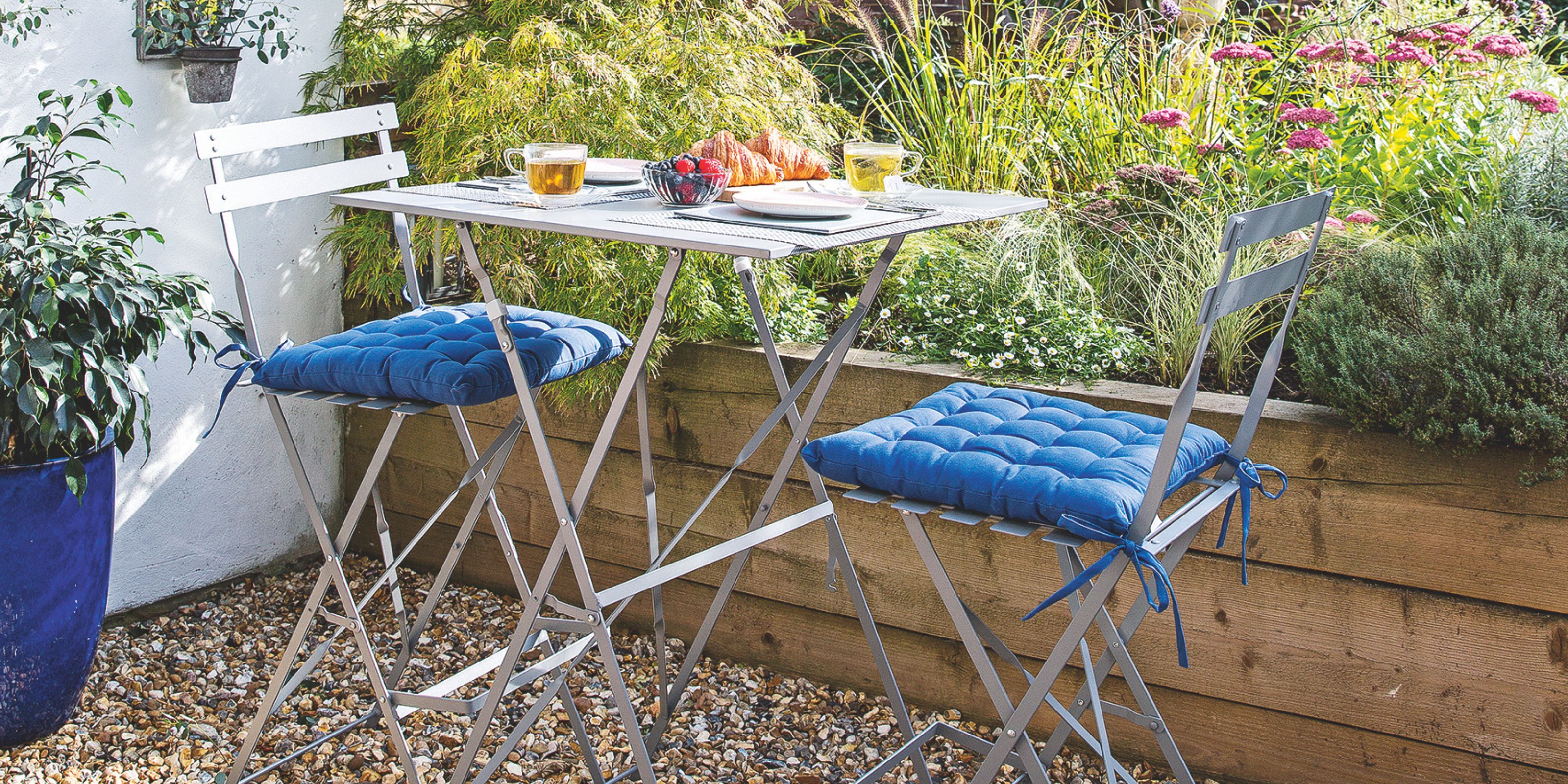 A metal bistro set in a stone garden in front of a wooden raised bed
