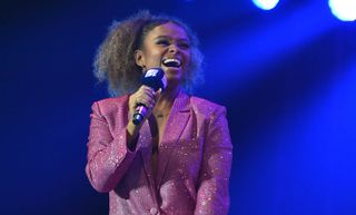 Joyfully smiling Fleur East in sparkly outfit with mic in hand.