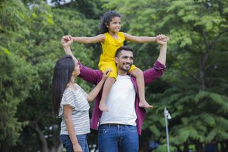 happy family in a park, father is carrying young daughter on his shoulders