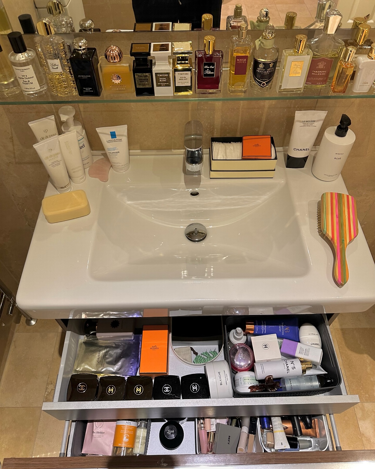 A sink filled with beauty products and perfume, including Amouage