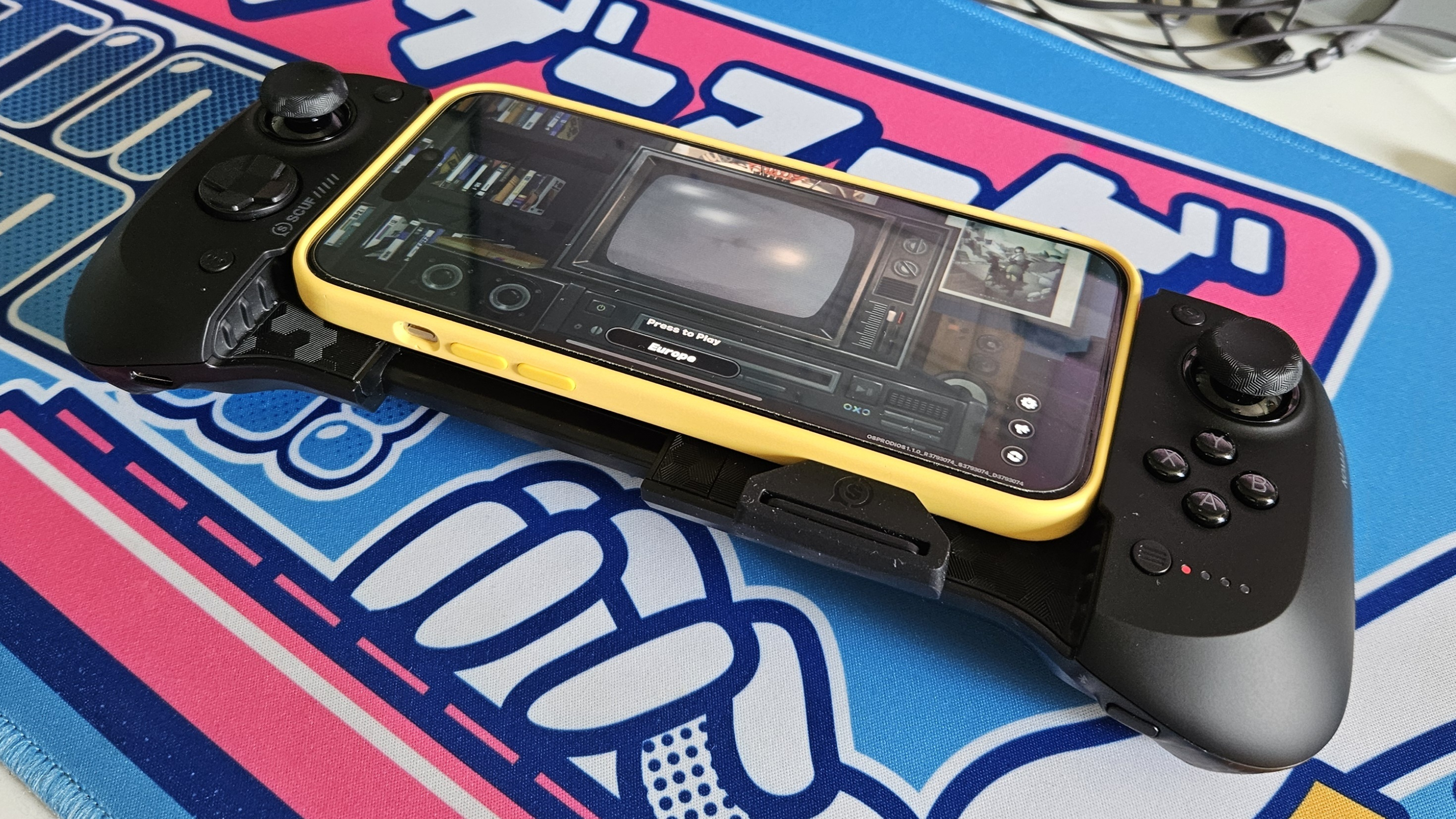 The Scuf Nomad and a mobile phone on a colorful desk mat.