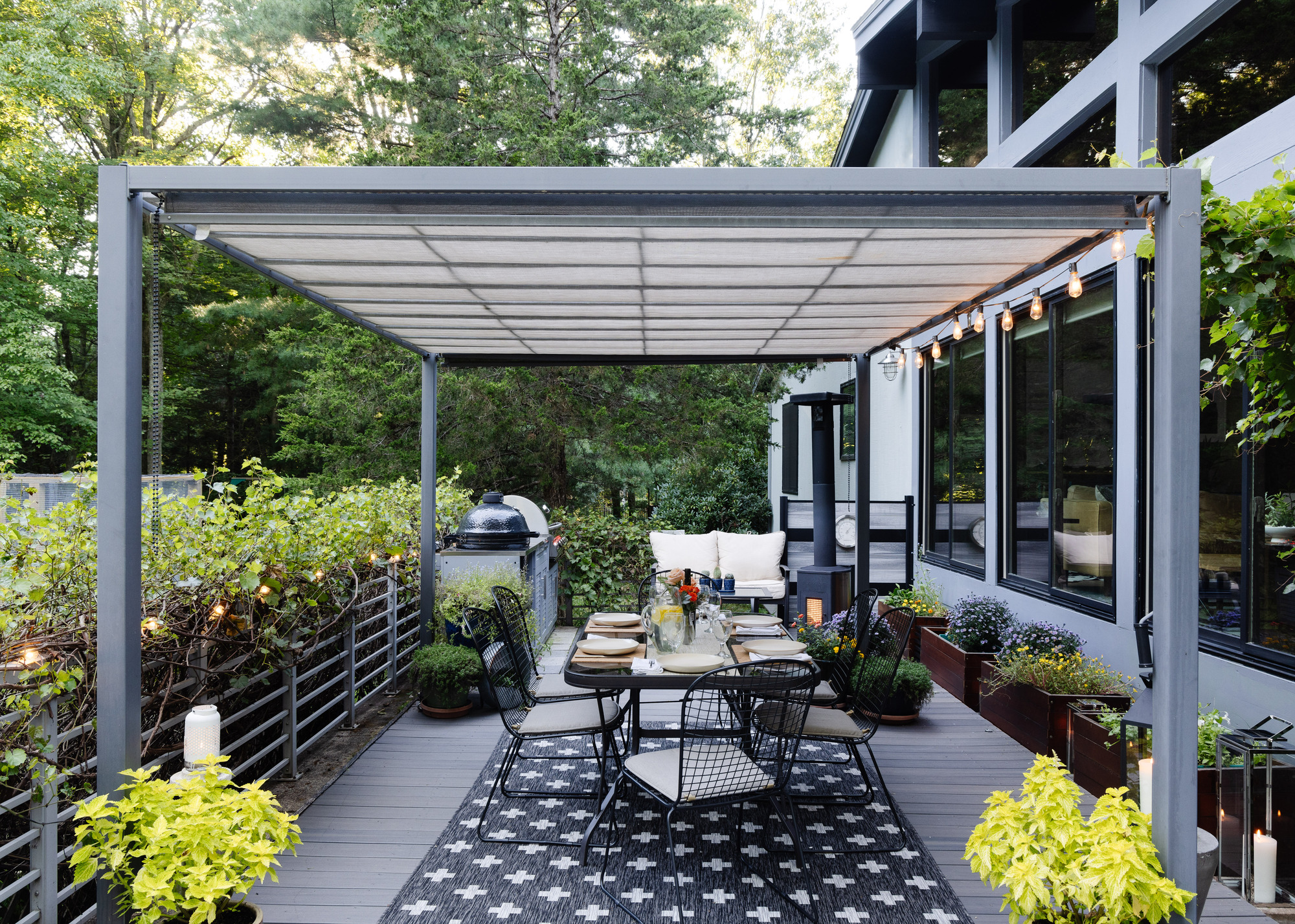 An outdoor deck with a pergola and a large dining table surrounded by potted plants and shrubs