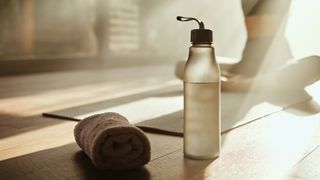 Water bottle and yoga towel sitting on wooden floor of the yoga studio with sunlight coming through window