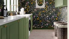A laundry room with green cabinets, a white washing machine, and bold black floral wallpaper
