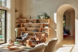Sitting area with magnolia limewash walls, wood bookshelf and brown leather armchairs