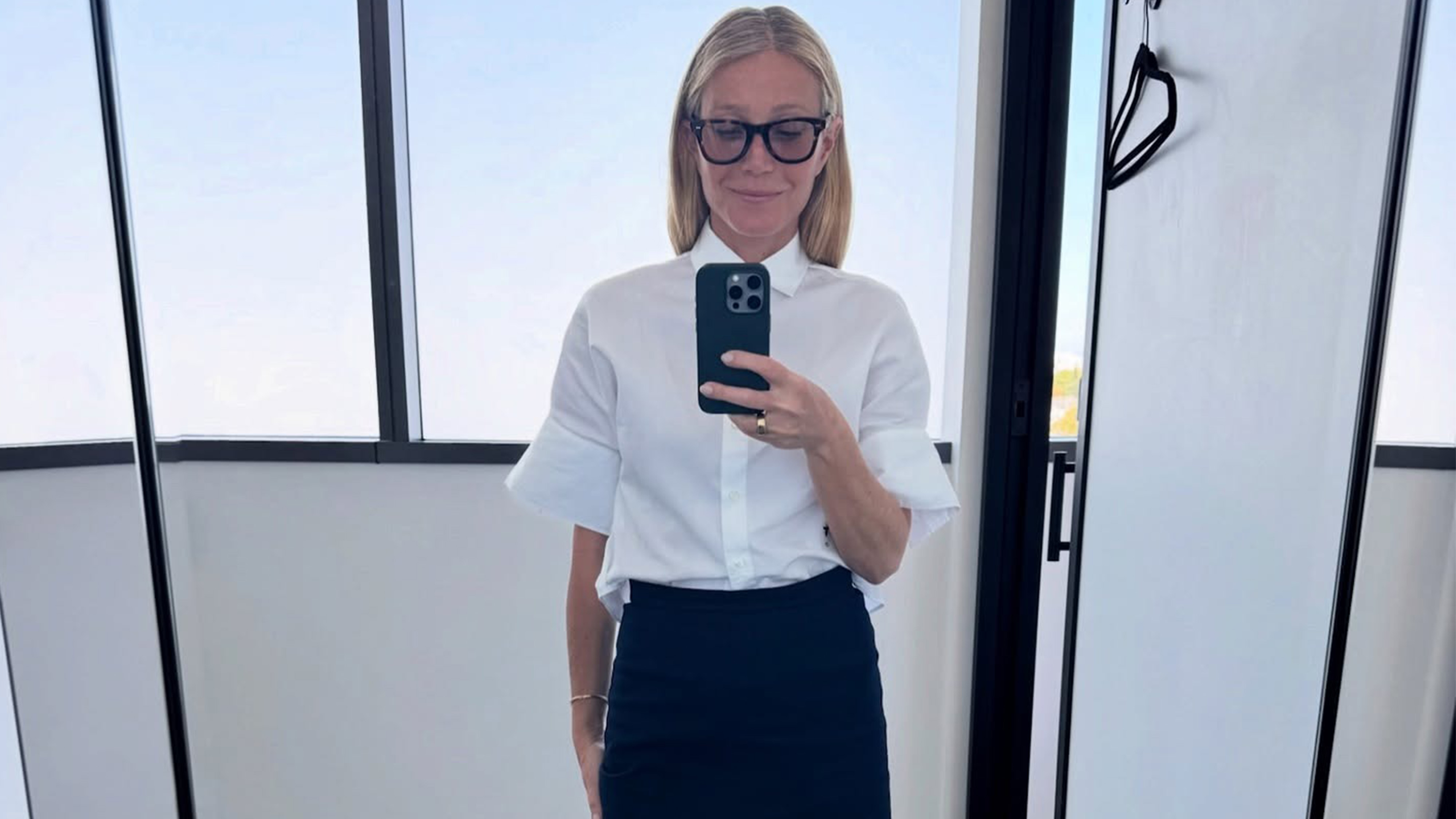 Gwyneth wears a white blouse, black midi skirt, and black Mary Janes.