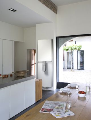 white kitchen with picture wall, white cabinetry, gray tiled floor, wooden table, radiator on wall