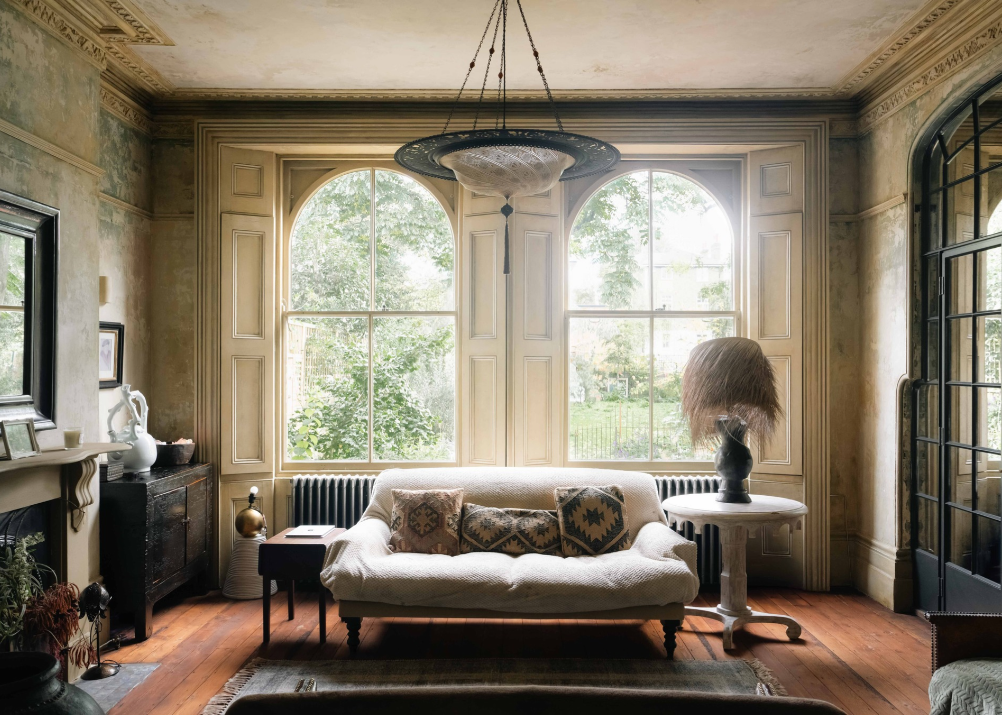 a dramatic sitting room with large arched windows, vintage aged walls, and antique furnishings