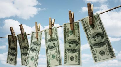 $100 bills dangle from a clothesline on a sunny day.