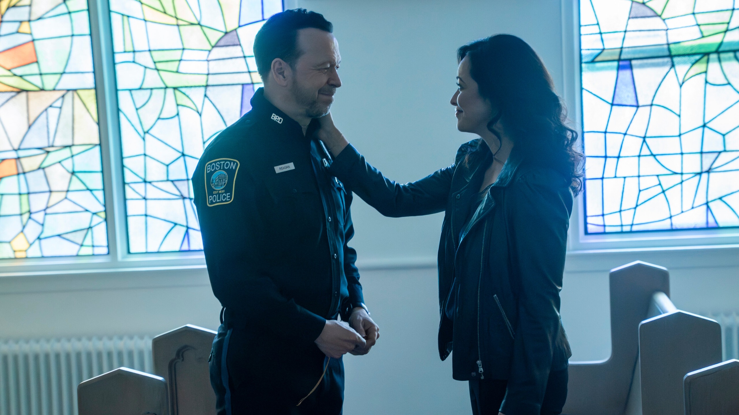 Maria Baez puts her hand on Danny Reagan's cheek and they smile at each other as they stand in a church.