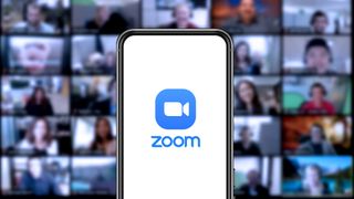 Zoom's logo on a mobile phone with screens of people in the background