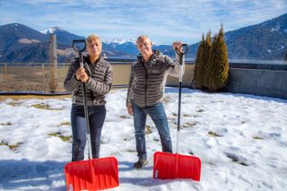 Monica and Rob bundled up and holding snow shovels in front of dramatic mountain backdrop.