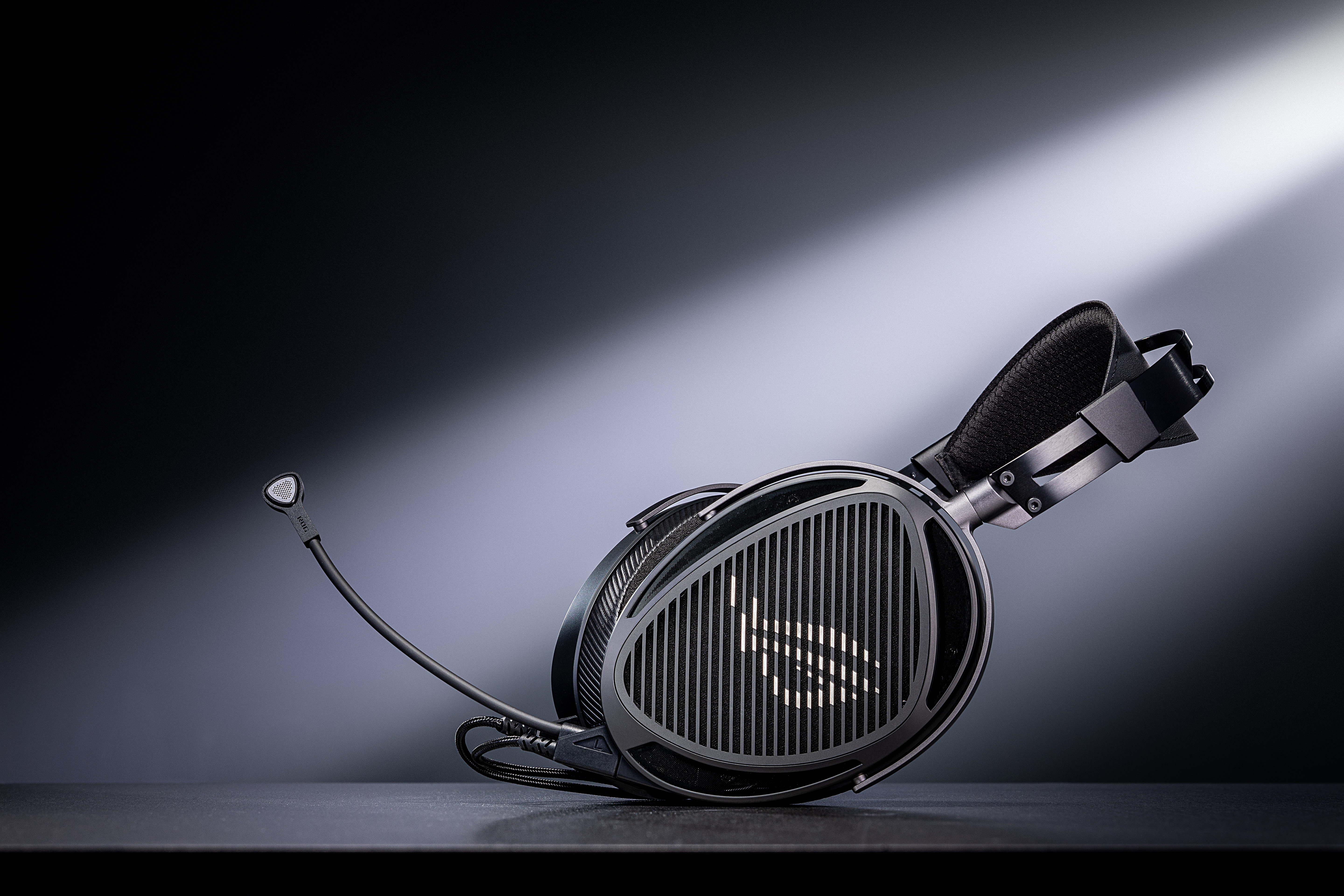 A side-profile view of the ROG Kithara gaming headset resting on a dark surface, highlighting its distinctive triangular earcups with a vertical grille design and a prominent boom microphone.