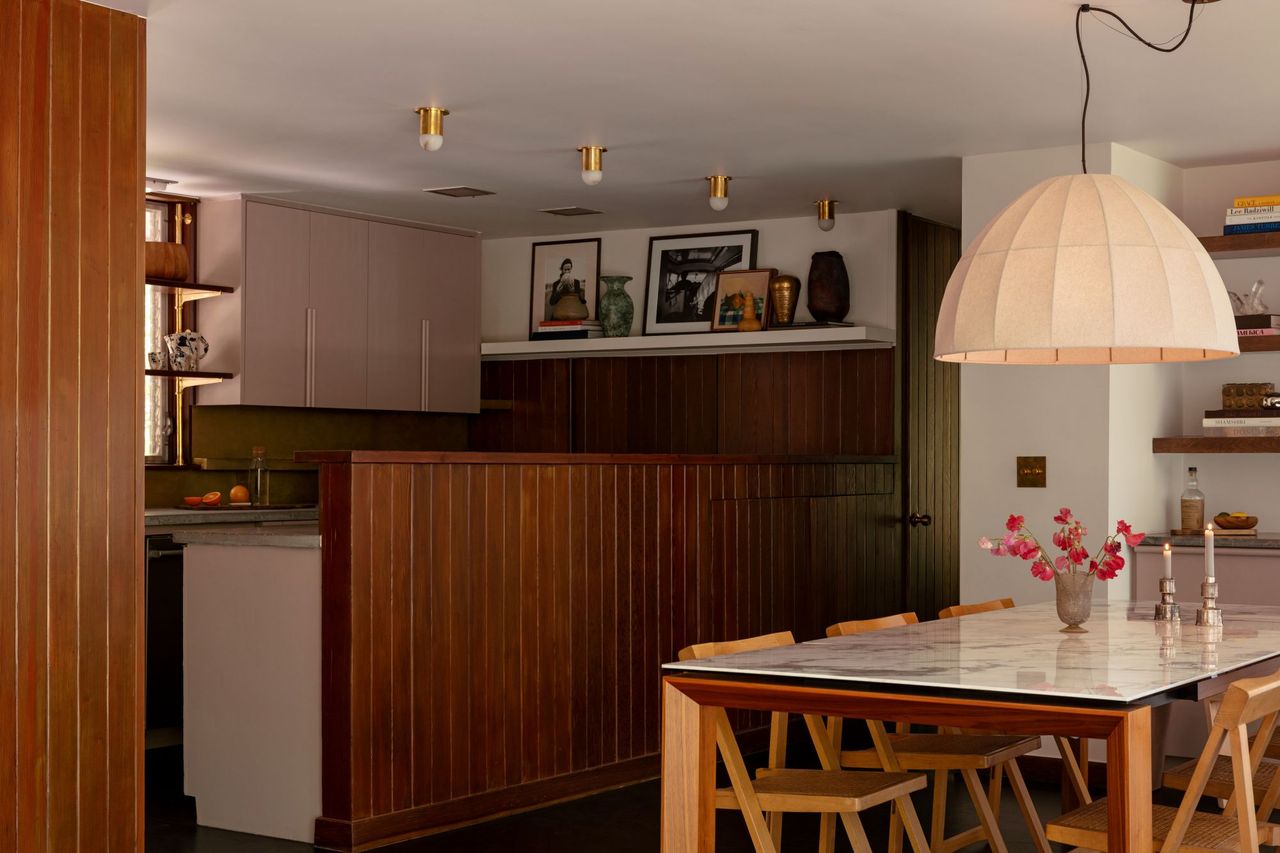 a kitchen and dining room with wood paneling, pink cabinets, a marble and wood dining table, and a large, organic pendant lamp