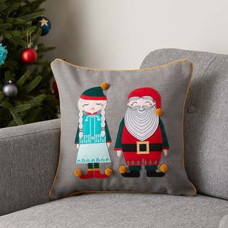 Grey Mr & Mrs Claus Christmas cushion on grey sofa with Christmas tree in background