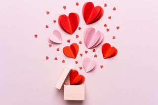 A pink gift box with red and pink hearts on a light pink background.