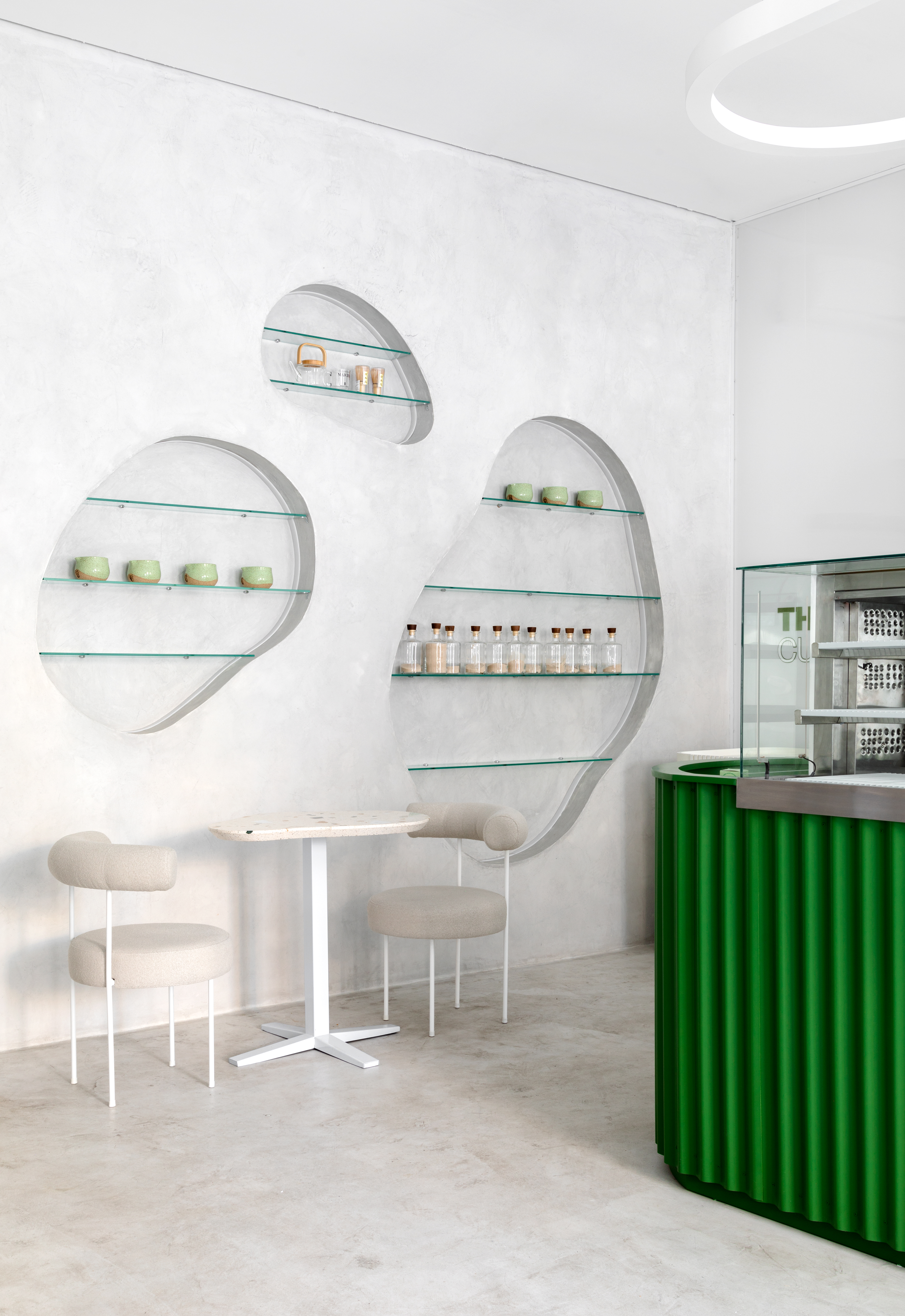 A white-washed, plastered matcha cafe with sculptural decor features monochromatic furnishings and an emerald green and chrome bar counter.