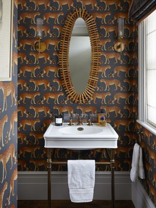 A bathroom covered in dark wallpaper with leopard prints with a mirror hanging centrally above the sink