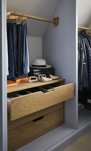 blue closet storage with wood shelving and rails, pant rail on one side, shirts on the other. space for shoe horns, hat, boxes.