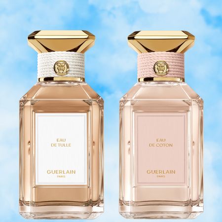 A woman wearing a white jacket and pants next to three bottles of Guerlain perfume. A blue sky cloud backdrop is behind them all. 