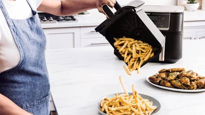 Someone tipping chips out of an air fryer basket onto a plate