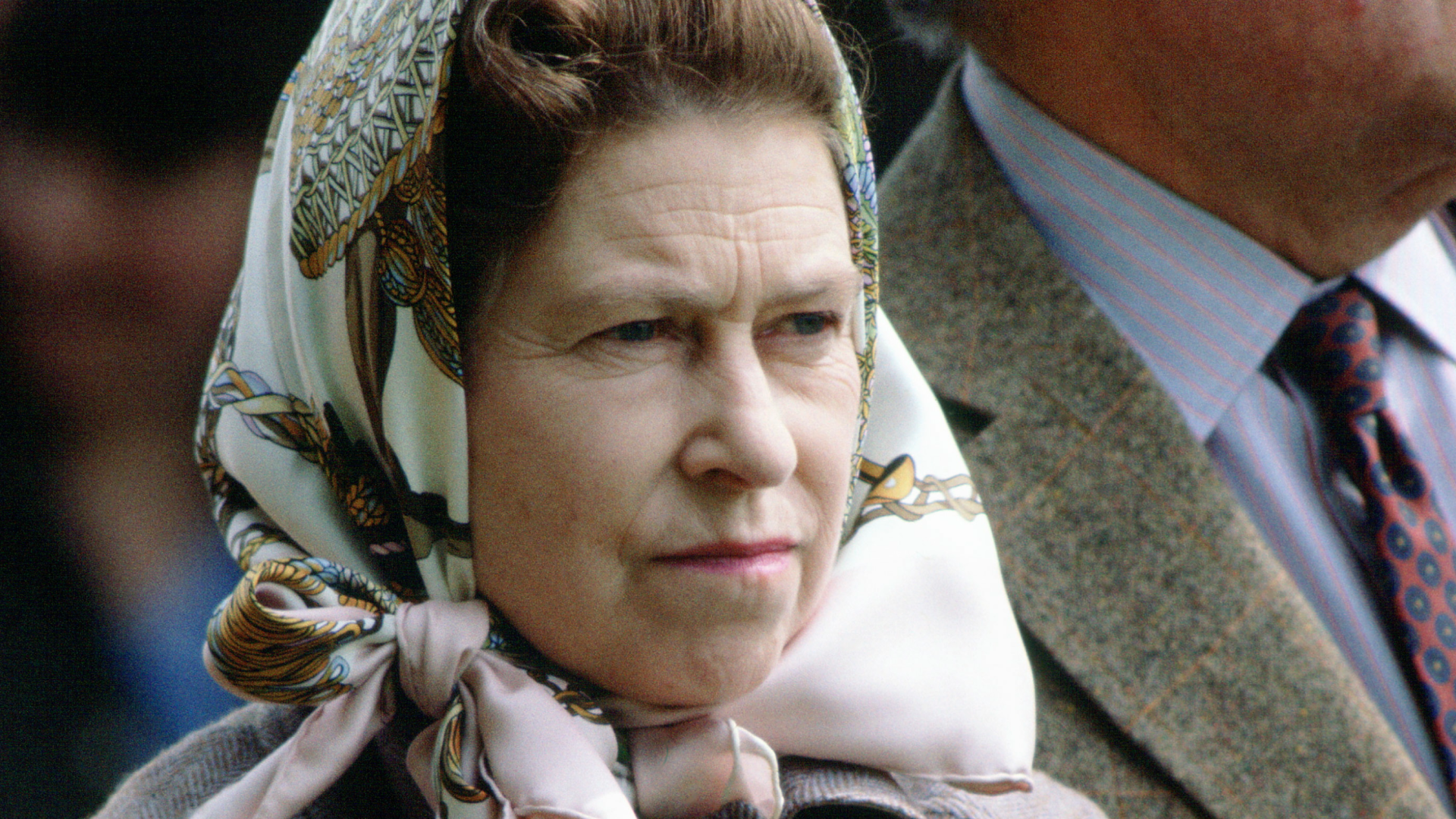 Queen Elizabeth wearing a head scarf and an angry expression