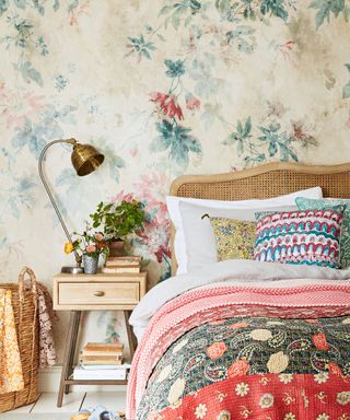 A floral country style bedroom with patterned bedlinen, a rattan headboard and a metal bedside lamp