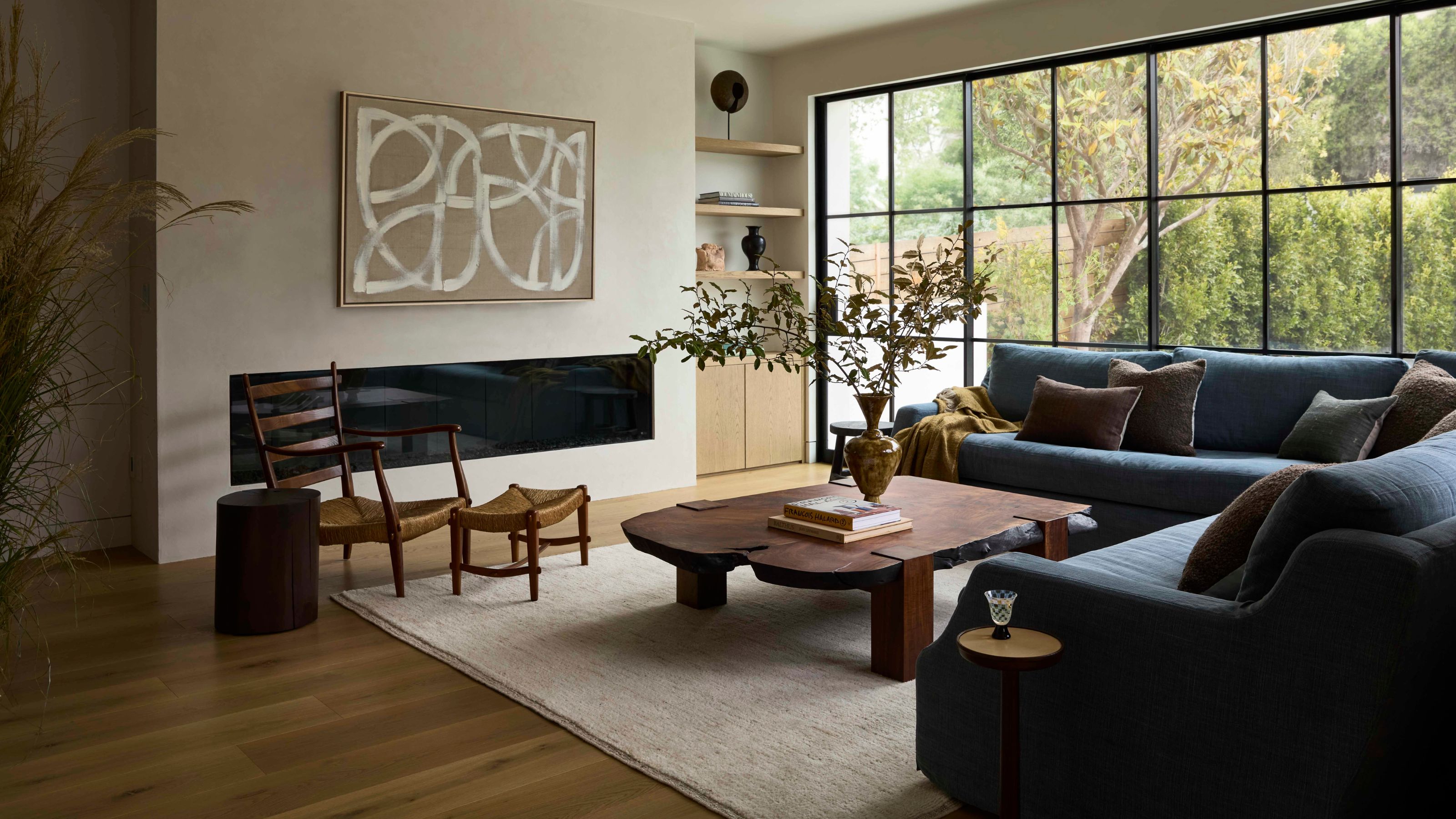 a wabi sabi family room with a modern fireplace and large crittal glass wall and navy sectional couch