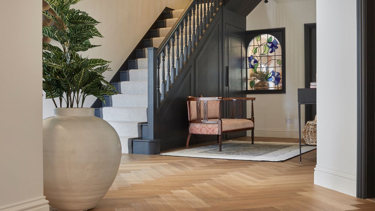 entrance hall with wooden flooring, grey staircase with cream runner, wooden chair on rug, stained glass window and large cream plant pot