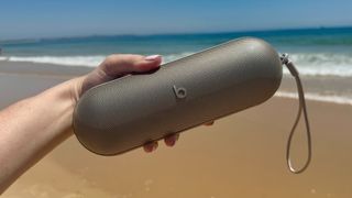 A hand holding the new Beats Pill 2024 in champagne in front of a beach