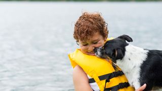 Young boy in yellow lifejacket swimming in the sea with a dog