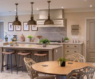 shaker style kitchen diner with stools around island unit as well as small round dining table with painted wooden chairs with ornate backs