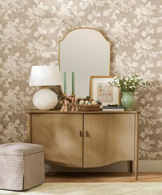 Console with green vase and flowers, wood cabinet, large mirror, egg picture, teal candles, and white lamp. Gingham ottoman sits underneath